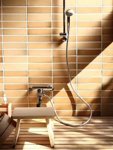 Stilvolles Badezimmer mit Holzbank, Handbrause und warmen Fliesen in der Dusche.