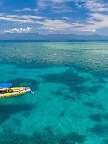 Kristallklares Wasser der Korallenriffe mit einem Boot im Hintergrund.