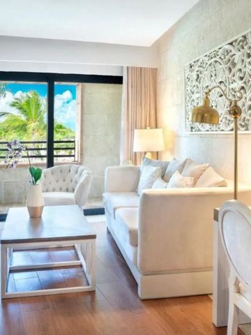 Wohnzimmer einer Suite mit heller Einrichtung und Blick auf Palmen.