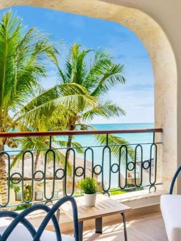 Balkon mit Sitzmöbeln und Meerblick durch Palmen.