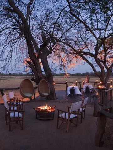 Abendliches Lagerfeuer mit Sitzbereich unter Bäumen in afrikanischer Wildnis