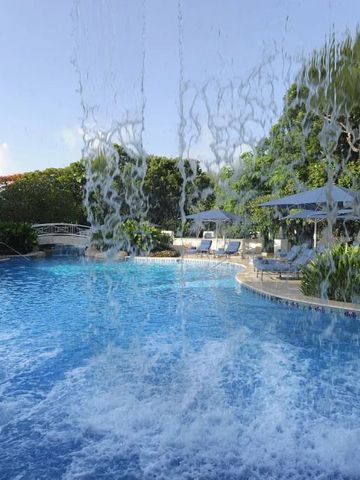Erfrischender Wasserfall am Pool mit Sonnenschirmen und Liegen im Hintergrund.