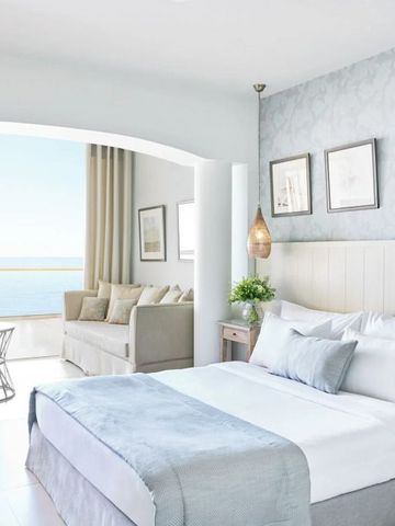 Helles Hotelzimmer mit Blick auf das Meer durch eine große Fensterfront.