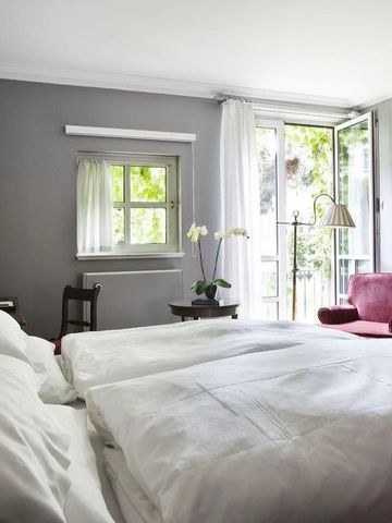 Geräumiges Hotelzimmer mit Doppelbett, geöffneten Fenstern und rotem Sessel