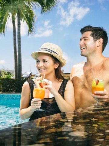 Paar genießt Drinks im Pool unter Palmen mit Meerblick