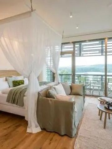 Helles Zimmer mit Himmelbett und Blick auf den See durch große Fenster.