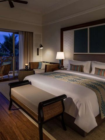 Geräumiges Hotelzimmer mit Doppelbett und Blick auf den Balkon bei Dämmerung.