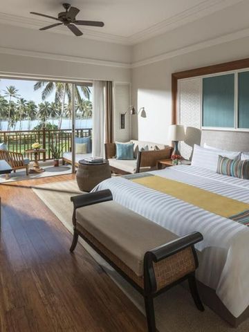 Helles Hotelzimmer mit Doppelbett und Balkon mit Palmenblick.