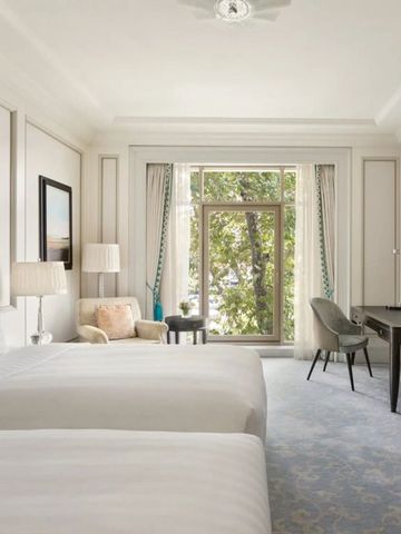 Helles Hotelzimmer mit zwei Betten und Blick auf Bäume und Wasser