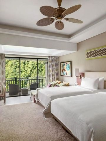 Hotelzimmer mit zwei Betten und großem Fenster mit Blick ins Grüne.