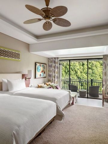 Geräumiges Doppelzimmer mit zwei Betten und Balkonblick auf tropische Vegetation.