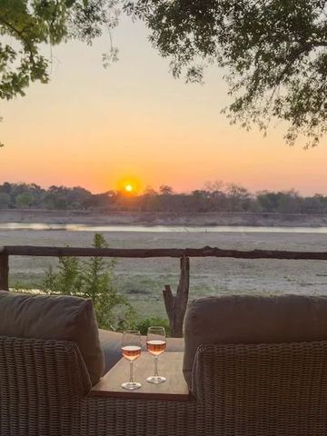 Sonnenuntergang mit zwei Gläsern Wein vor Flusslandschaft.