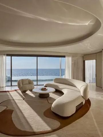 Eleganter Wohnraum mit geschwungener Couch und direktem Blick auf das Meer.
