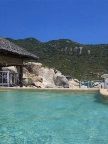 Kristallklarer Privatpool mit Strohdach und Hügeln im Hintergrund