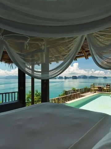 Blick von einem Bett auf das Meer und die umliegenden Inseln durch weit geöffnete Fenster