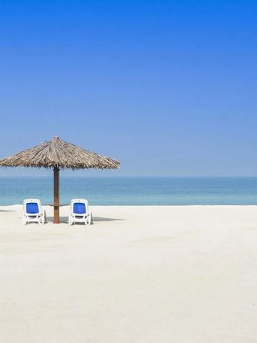 Weißer Sandstrand mit Strohschirmen und Liegestühlen am klaren Meer