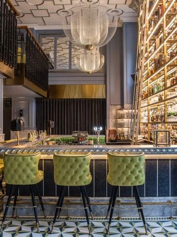 Elegante Hotelbar mit grünen Barhockern und beleuchtetem Flaschenregal im Sofitel Legend Metropole Hanoi