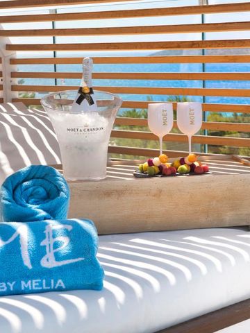 Sonnenliege mit Handtuch und Champagner vor Meereshintergrund.