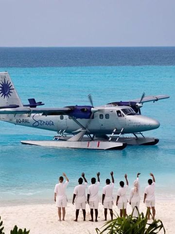 Wasserflugzeug landet im türkisblauen Meer vor einem Strand