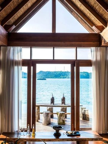 Blick aus einer Villa mit Holzdecke auf das Meer und eine Terrasse mit rustikalen Möbeln