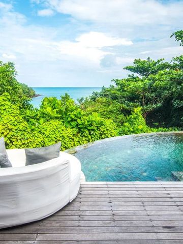 Holzterrasse mit weißem Sofa und Blick auf tropische Vegetation und Meer