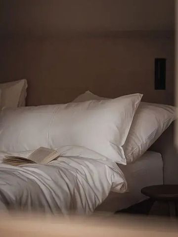 Gemütliches Bett mit hochwertiger Bettwäsche und offenem Buch.