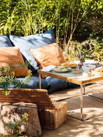 Gemütliche Sitzecke im Freien mit Kissen und Tisch, umgeben von grüner Natur
