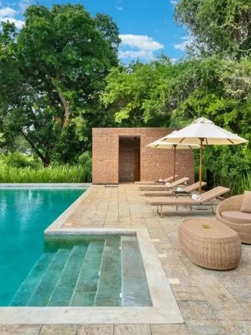 Poolbereich mit Liegen und Sonnenschirmen in grüner Gartenumgebung