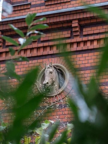 Rote Backsteinfassade mit Skulptur eingerahmt von grünen Blättern