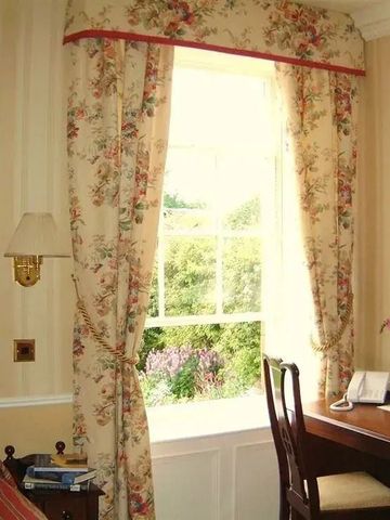 Helles Fenster mit Blumenvorhängen und Schreibtisch im Hotelzimmer