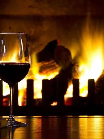 Zwei Weingläser vor einem knisternden Kamin.