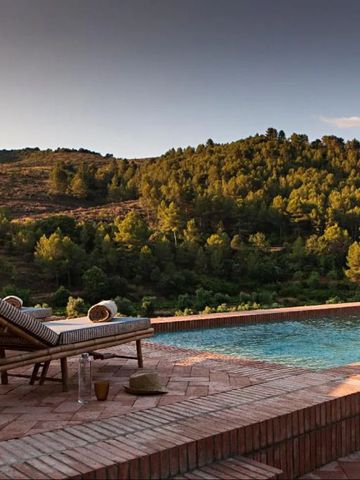 Infinity Pool mit Sonnenliegen umgeben von grüner Hügellandschaft