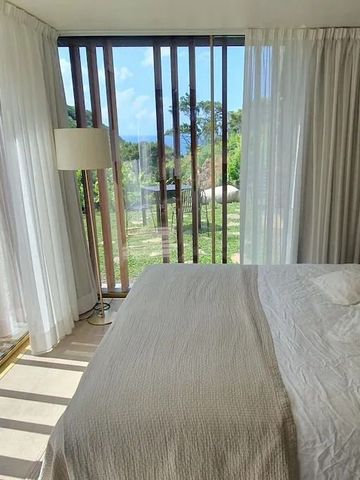 Schlafzimmer mit Fensterfront und Aussicht auf Garten und Berge.