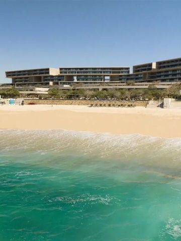 Strandansicht mit türkisfarbenem Wasser und Hotelgebäude im Hintergrund