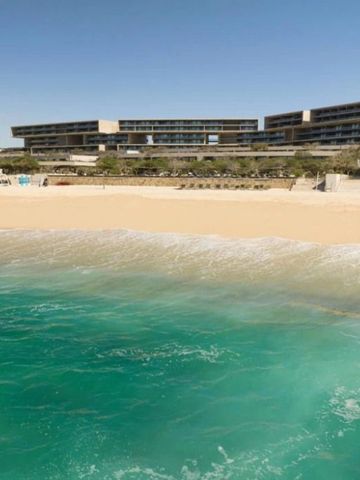 Strand mit welligem Wasser und Hotelgebäude unter klarem Himmel