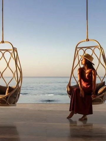 Frau in Hängesessel mit Blick aufs Meer während des Sonnenuntergangs