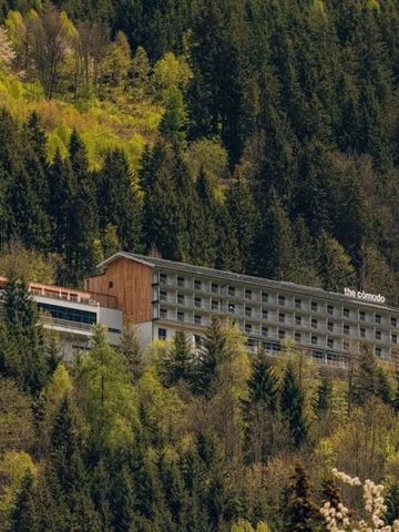 Hotelgebäude umgeben von Wald und Bergen in alpiner Landschaft