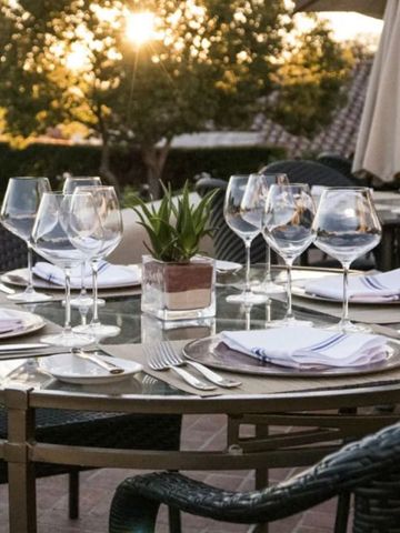 Eleganter Terrassentisch mit Glaswaren und Tischgedeck im Sonnenuntergang.