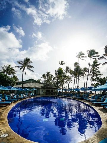 Poollandschaft mit blauen Liegen und Palmen unter sonnigem Himmel