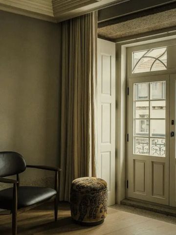 Stilvolles Zimmer mit klassischem Stuhl und elegantem Hocker vor einem großen Fenster.