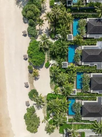 Luftaufnahme von Villen mit Pools am Strand unter Palmen.