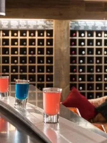 Elegante Bar mit farbigen Shots und beeindruckendem Weinkeller im Hintergrund.