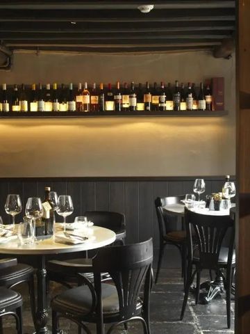 Gemütlicher Essbereich mit Tischen, Weingläsern und Flaschenregal an der Wand