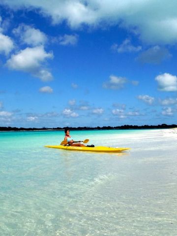 Person auf einem gelben Kajak im klaren türkisfarbenen Wasser am Strand