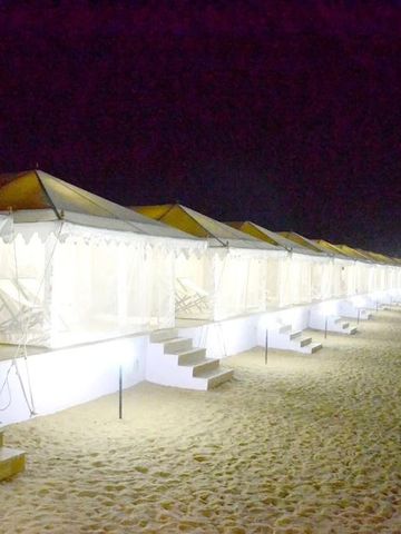 Reihe von beleuchteten Luxuszelten bei Nacht auf einem Sandstrand.