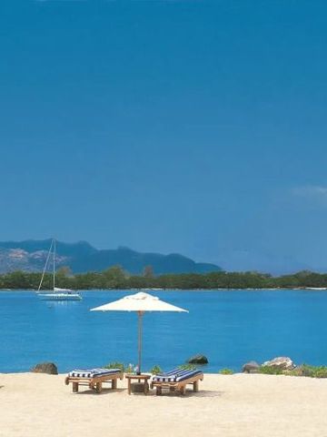 Strand mit Liegestühlen und Sonnenschirmen, türkisblaues Meer im Hintergrund