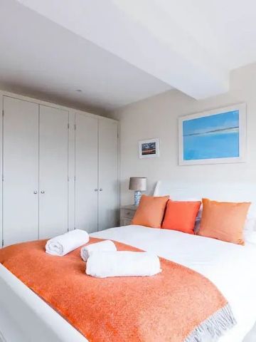 Minimalistisches Schlafzimmer mit Doppelbett, orangen Kissen und großem Schrank.