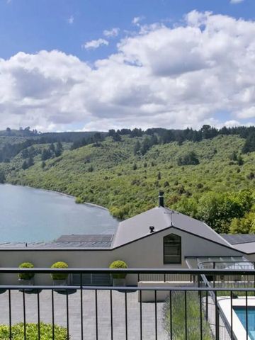 Blick auf einen See und bewaldete Hügel von einer Terrasse mit Pool