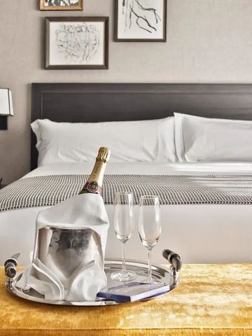 Luxuriöses Hotelzimmer mit Sekt auf Tablett vor einladendem Bett.