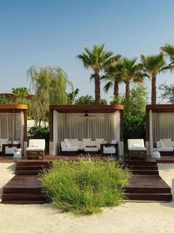 Strandbereich mit eleganten Cabanas und Palmen vor blauem Himmel